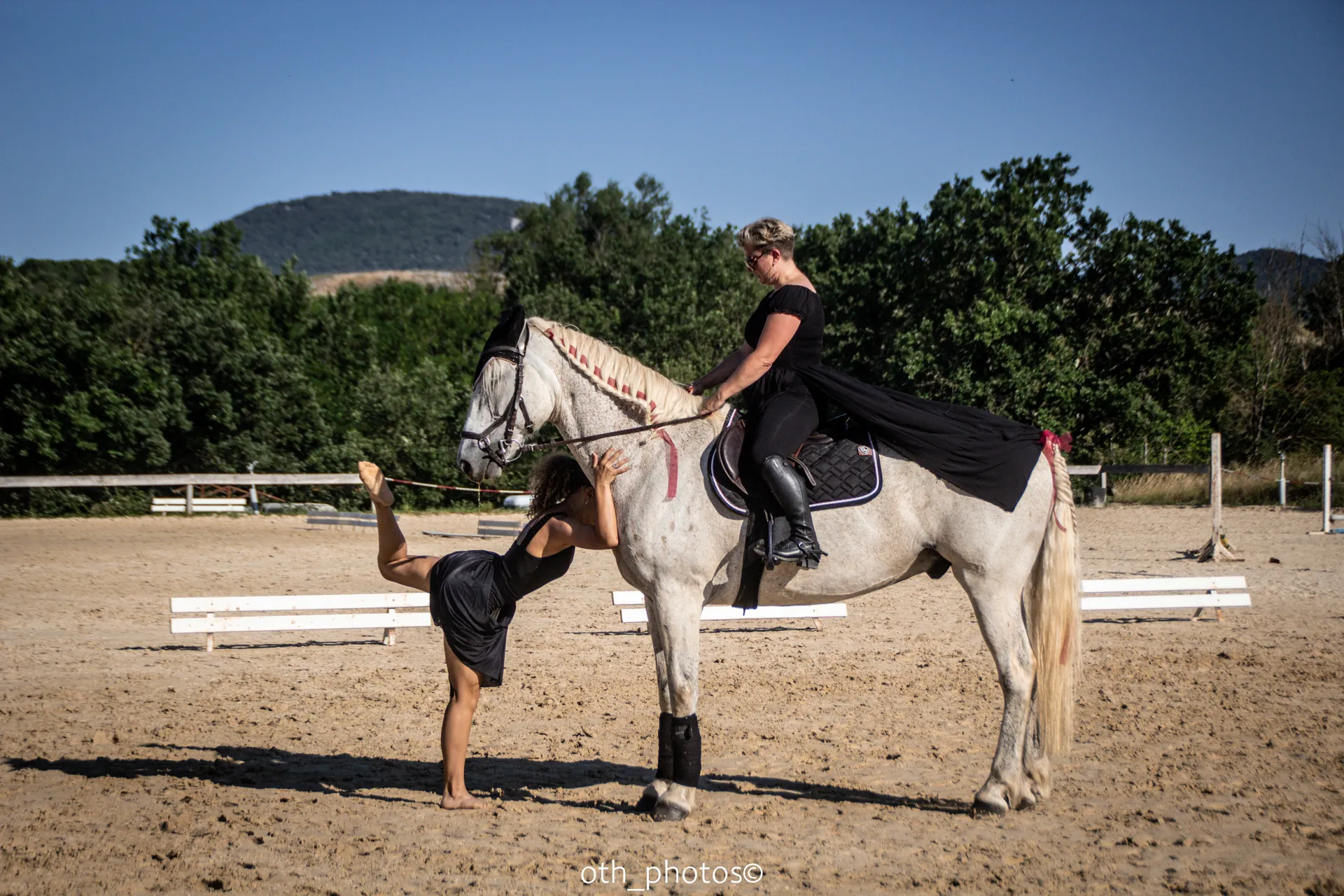 Une scène de spectacle équestre avec un cheval gris et deux participantes en tenue noire