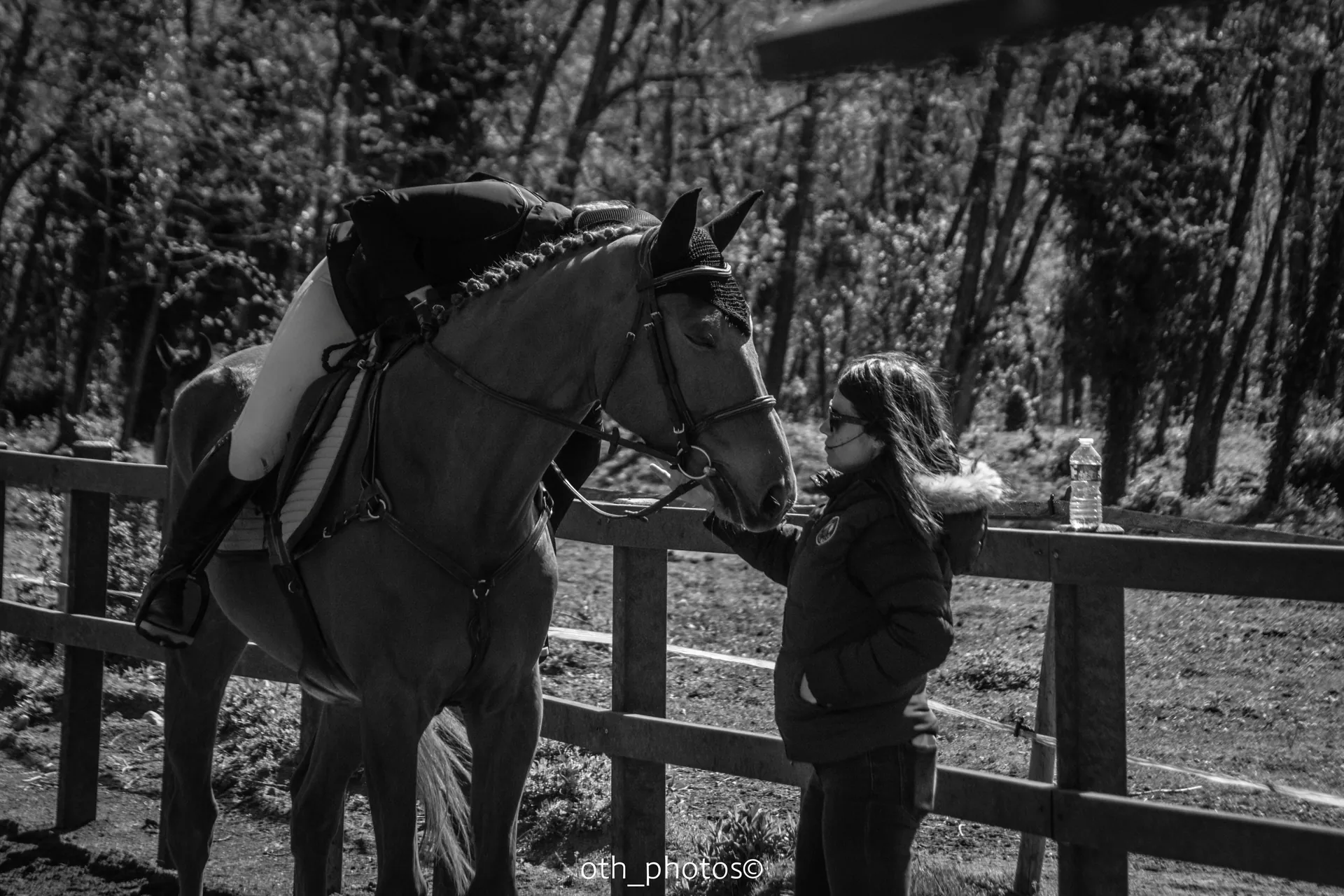 Photographie en noir et blanc d’une cavalière penchée sur l’encolure de son cheval, près d’une accompagnatrice