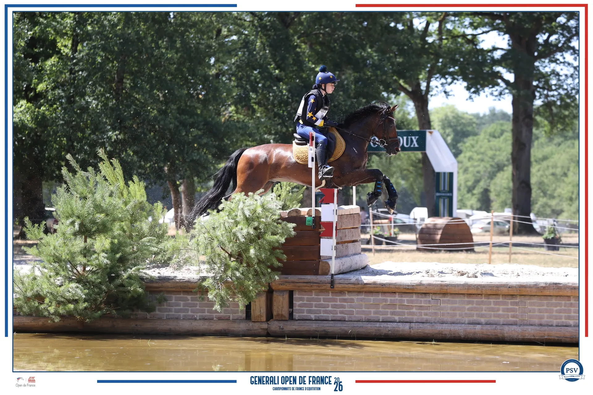 Une cavalière et son cheval bai en plein saut au-dessus d’un obstacle de cross bordé d’eau