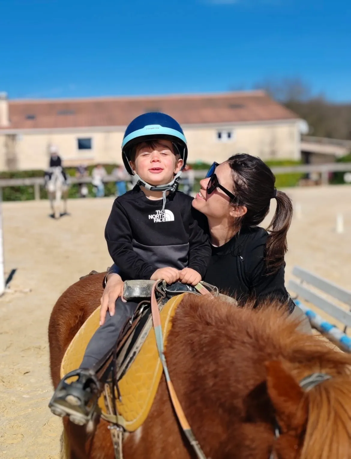 Un jeune enfant casqué sur un poney, accompagné d’une adulte à ses côtés
