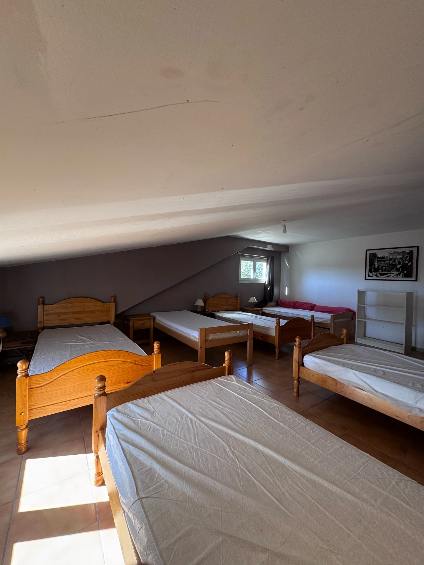 Des lits individuels en bois alignés dans le dortoir lumineux du gîte