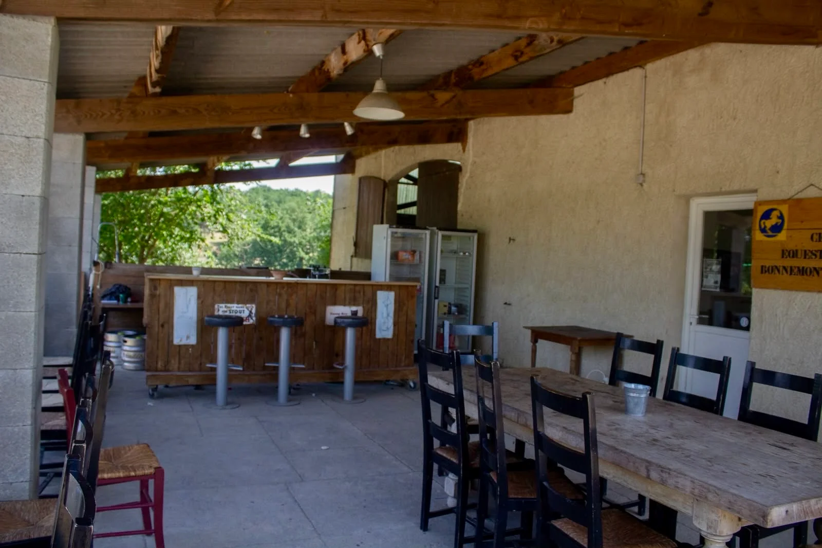 Le bar en bois et ses tabourets sous la terrasse couverte, près d’une grande table